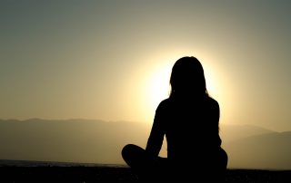 Frau meditiert vor Sonnenuntergang